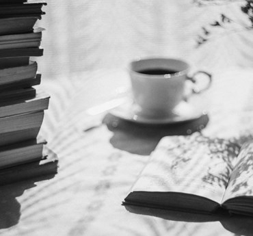 Svartvitt foto av en kaffekopp, till vänster en trave tummade böcker.